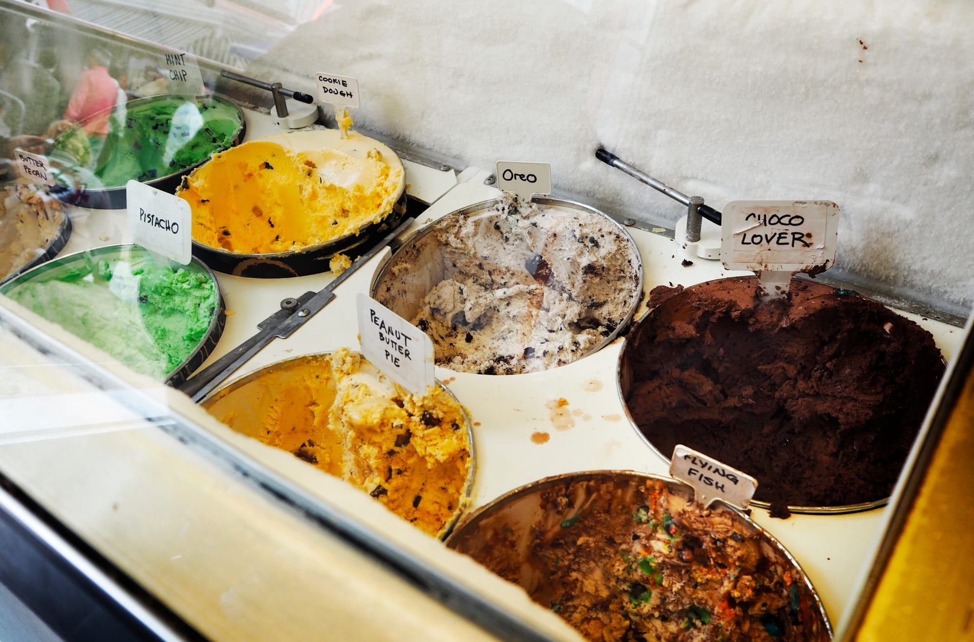 Tubs of ice cream with handwritten flavor labels in a glass case