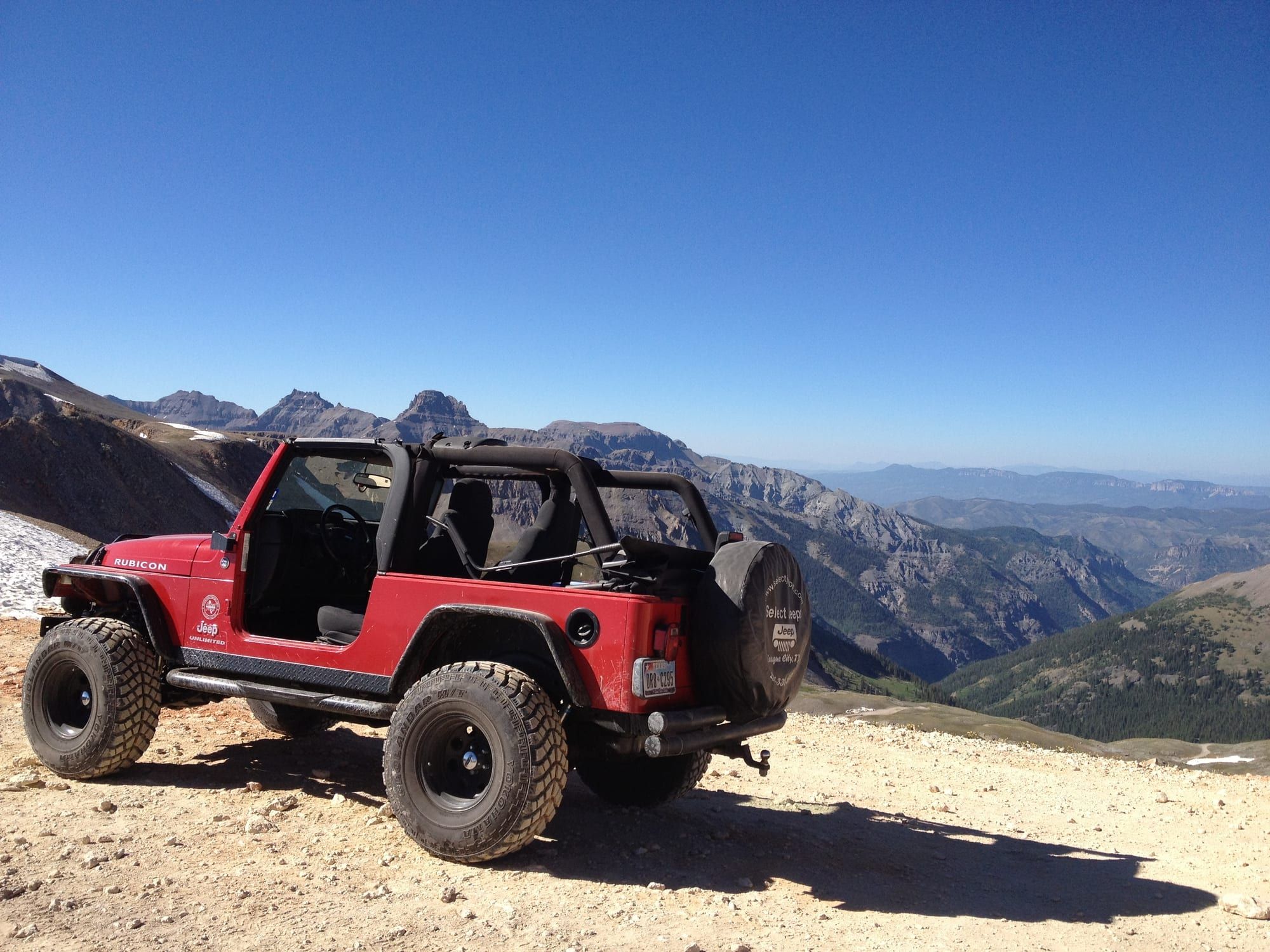 A red Jeep at the top of Imogene Pass, with peaks beyond