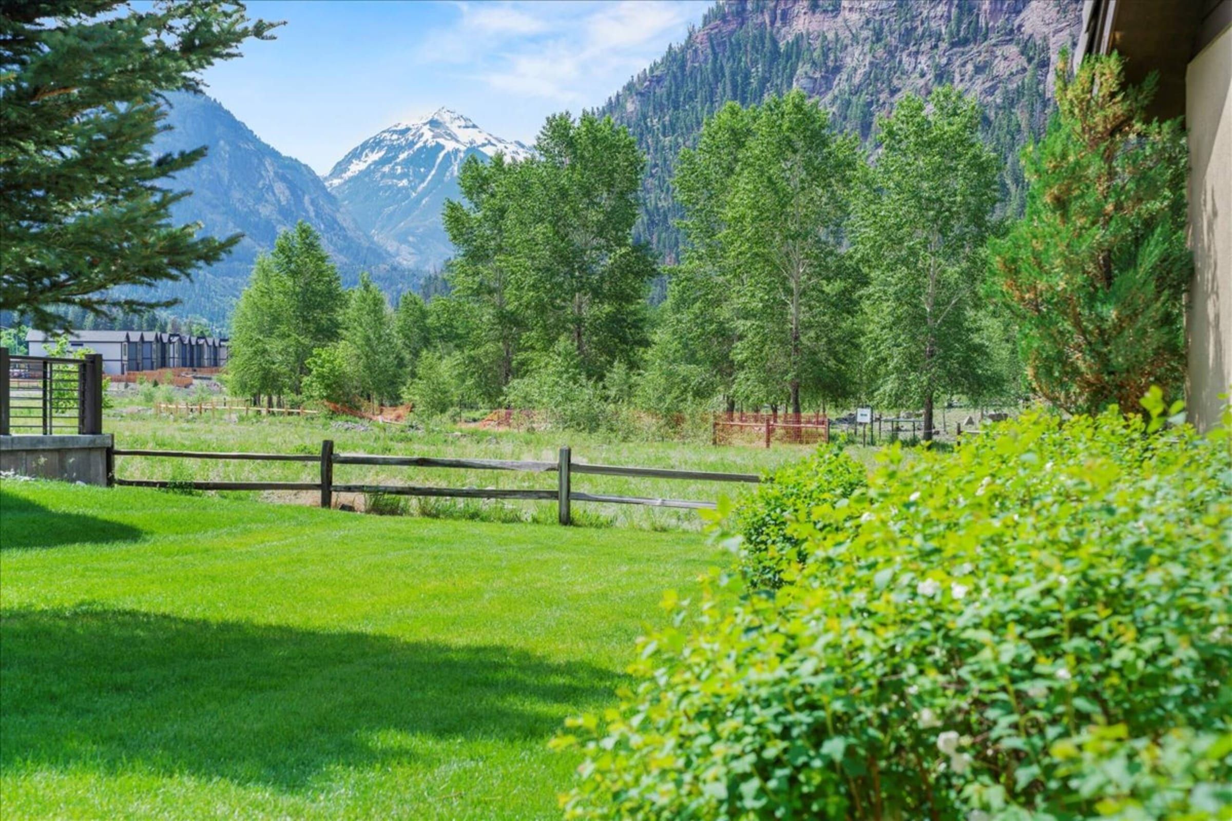 The lawn and split-rail fence below a snowcapped peak