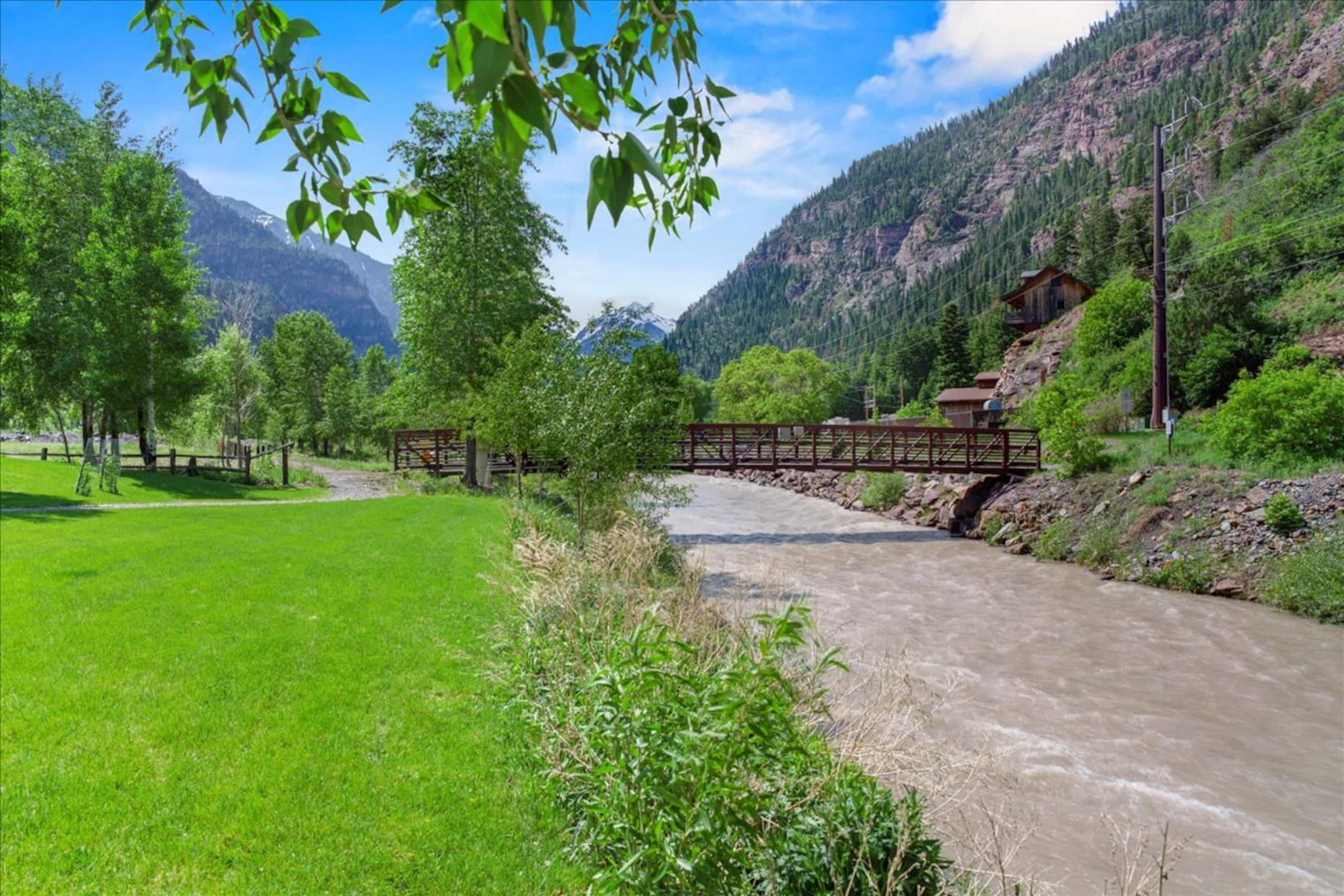 The Uncompahgre River beside the back lawn, with the Riverwalk footbridge and the peaks beyond